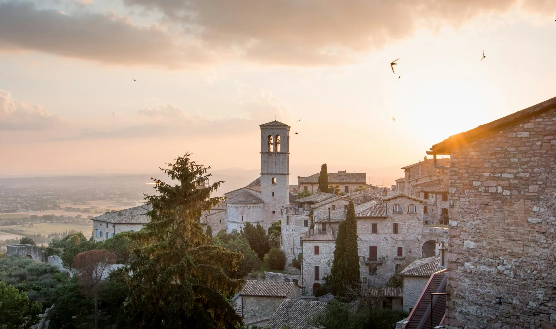 Assisi's stone bell tower glowing over the Umbrian valley at sunset