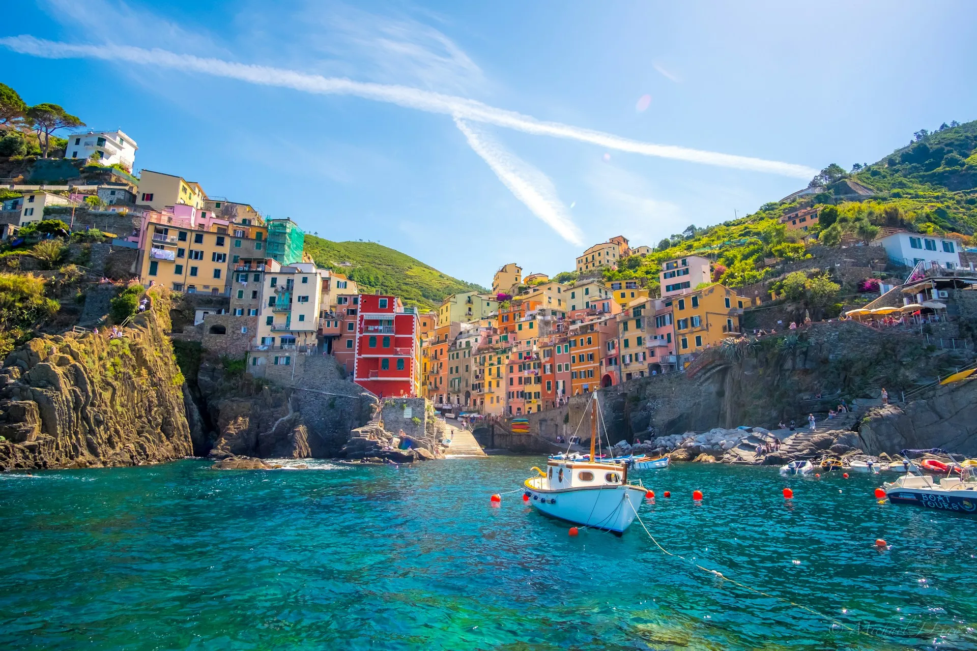 Riomaggiore's coloured houses stacked above a turquoise cove, a small boat moored in the clear water