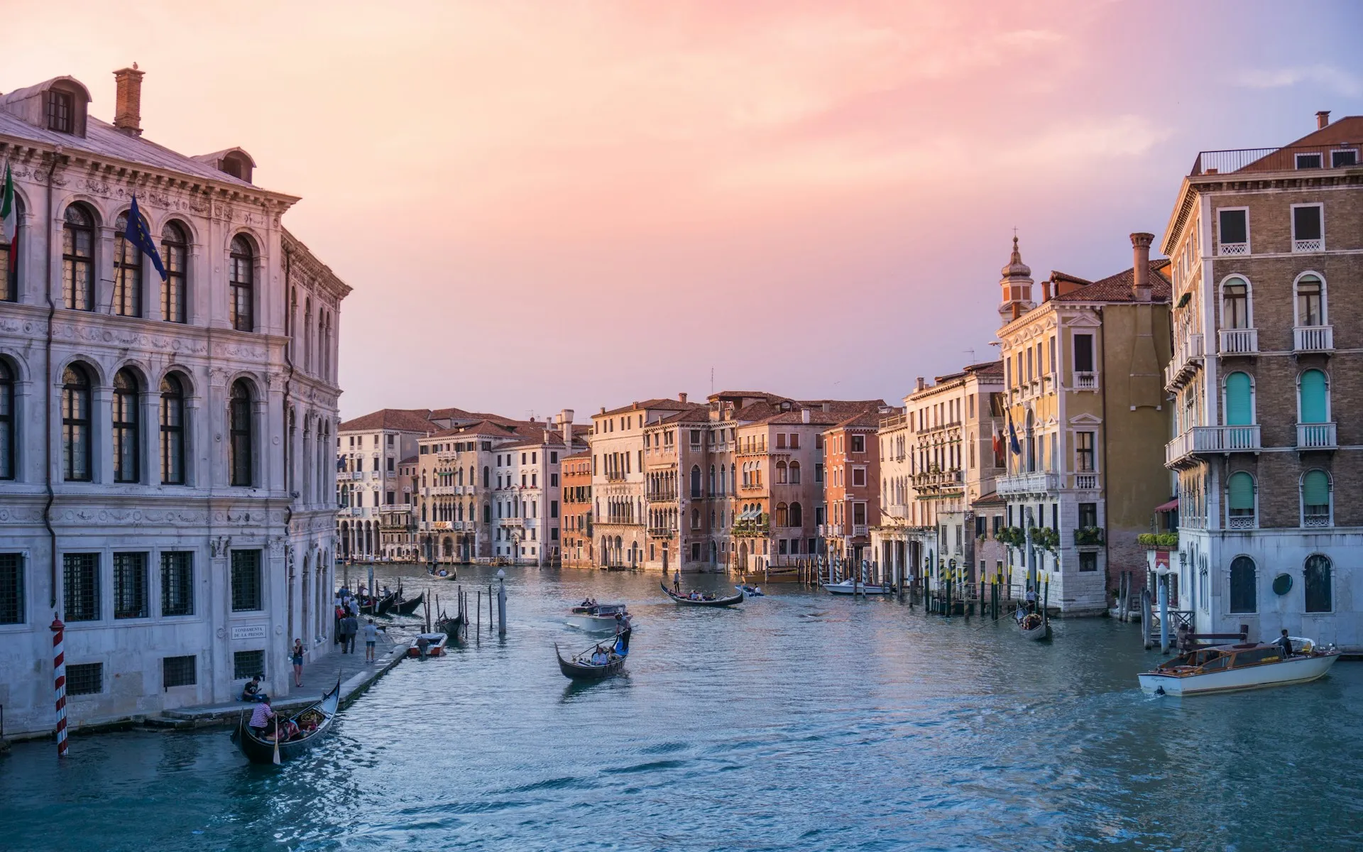 Venice's Grand Canal at dusk, gondolas gliding between the palazzi under a rose-coloured sky