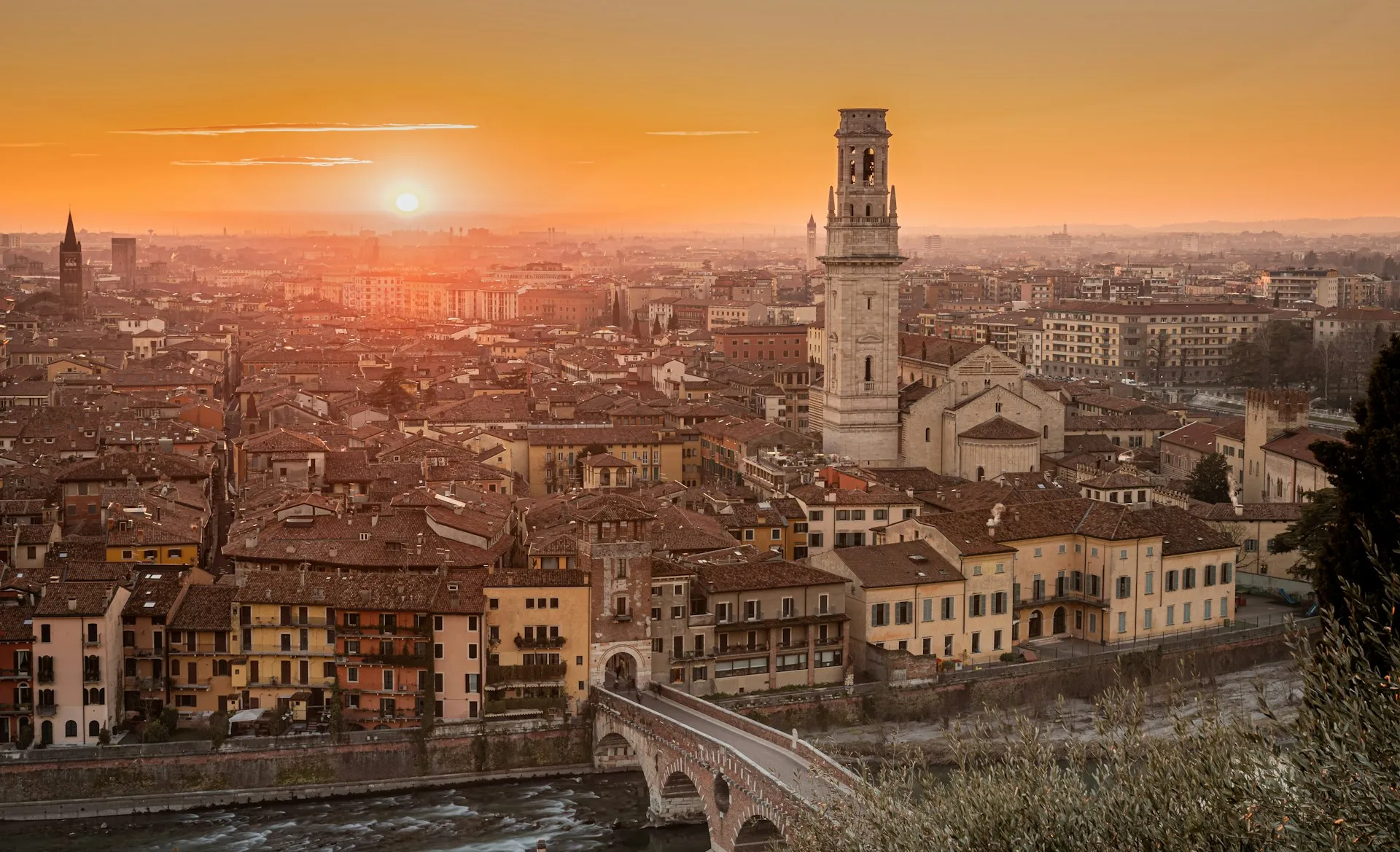 Verona glowing at sunset — the cathedral bell tower and the Ponte Pietra over a bend in the Adige