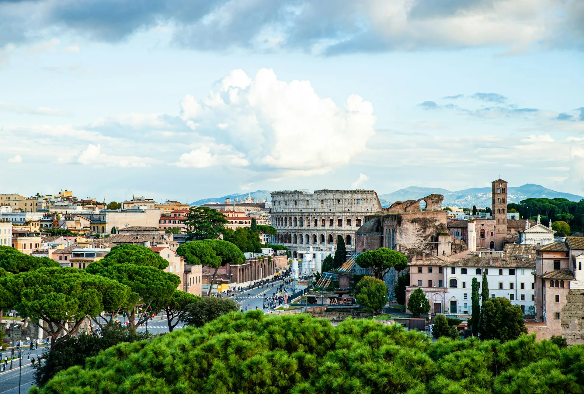 The Colosseum rising above Rome's rooftops and umbrella pines under a towering sky