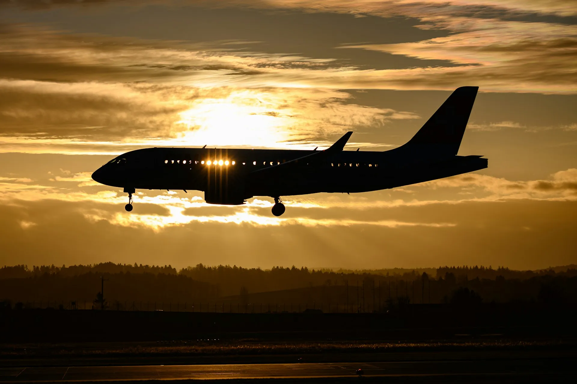 A plane on final approach at golden hour, the setting sun burning through its cabin windows — the journey begins